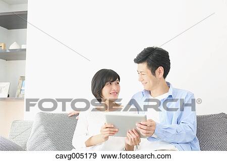 Stock Photo - Japanese couple on the sofa with tablet. Fotosearch