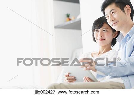 Stock Photo - Japanese couple on the sofa with tablet. Fotosearch