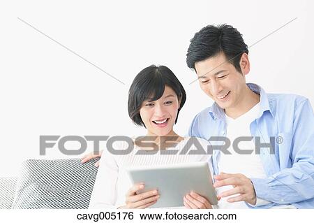 Stock Photograph - Japanese couple on the sofa with tablet. Fotosearch