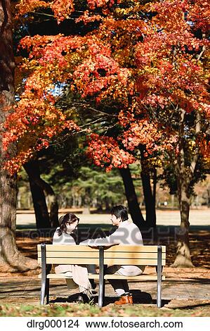Picture - Senior Japanese couple sitting on a bench in a city park. Fotosearch