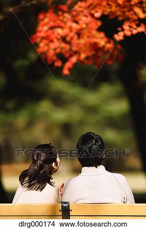 Picture - Senior Japanese couple sitting on a bench in a city park. Fotosearch