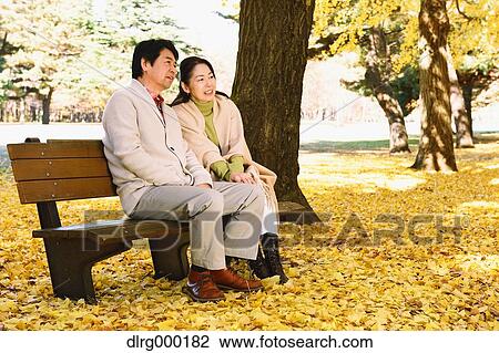 Stock Image - Senior Japanese couple sitting on a bench in a city park. Fotosearch