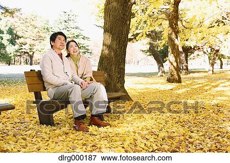 Stock Photo - Senior Japanese couple sitting on a bench in a city park. Fotosearch