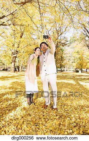 Stock Photograph - Senior Japanese couple taking pictures in a city park in Autumn. Fotosearch