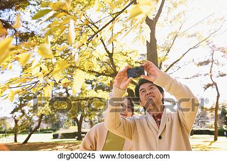 Stock Photography - Senior Japanese couple taking pictures in a city park in Autumn. Fotosearch