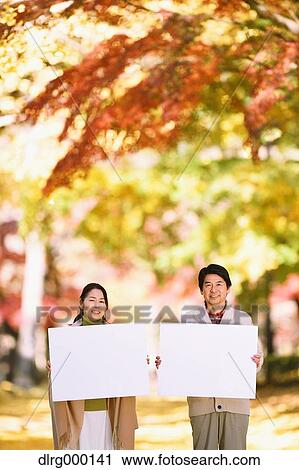 Stock Image - Senior Japanese couple with whiteboard in a city park. Fotosearch