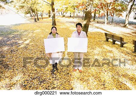 Stock Image - Senior Japanese couple with whiteboard in a city park. Fotosearch
