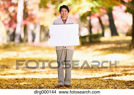 Picture - Senior Japanese man with whiteboard in a city park in Autumn. Fotosearch