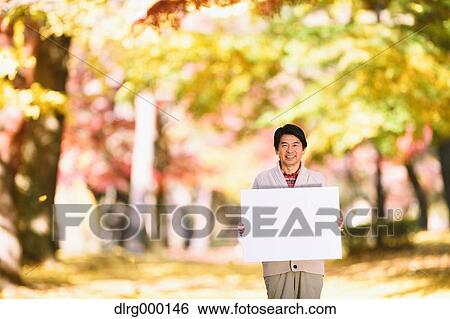 Stock Photograph - Senior Japanese man with whiteboard in a city park in Autumn. Fotosearch