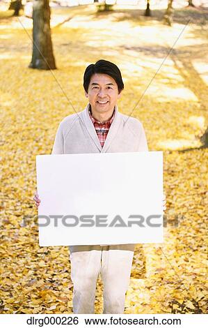 Stock Photograph - Senior Japanese man with whiteboard in a city park in Autumn. Fotosearch