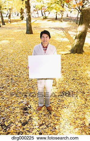 Stock Photography - Senior Japanese man with whiteboard in a city park in Autumn. Fotosearch