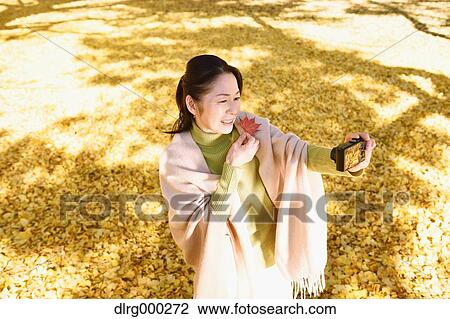 Stock Image - Senior Japanese woman taking a selfie in a city park in Autumn. Fotosearch