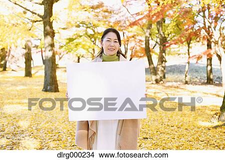 Picture - Senior Japanese woman with whiteboard in a city park in Autumn. Fotosearch