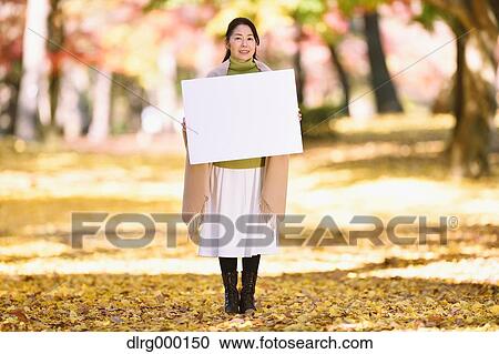 Stock Image - Senior Japanese woman with whiteboard in a city park in Autumn. Fotosearch