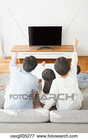 Stock Photo - Young Japanese family watching TV in the living room. Fotosearch