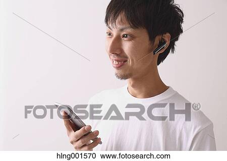 Stock Image - Young Japanese man using smartphone with wireless earphone. Fotosearch
