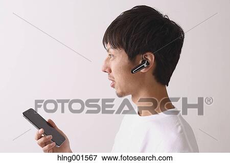 Stock Photo - Young Japanese man using smartphone with wireless earphone. Fotosearch