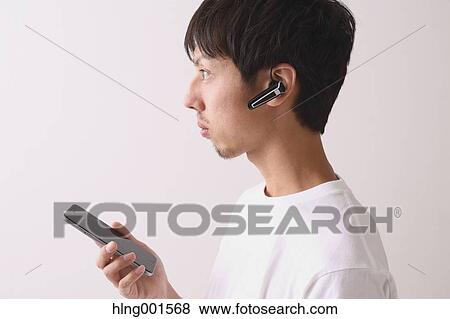 Stock Photo - Young Japanese man using smartphone with wireless earphone. Fotosearch