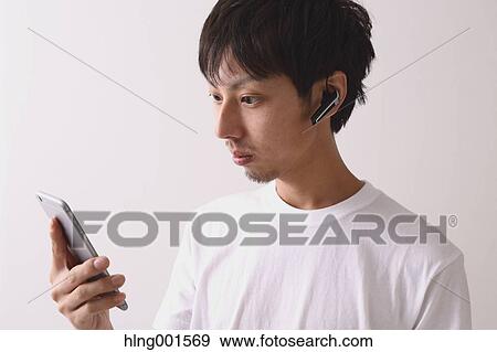Stock Photo - Young Japanese man using smartphone with wireless earphone. Fotosearch