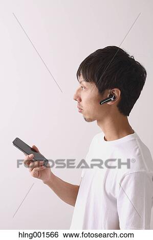 Stock Photograph - Young Japanese man using smartphone with wireless earphone. Fotosearch