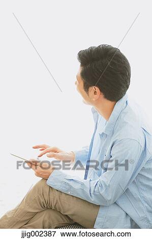Stock Photo - Young Japanese man with tablet on the sofa. Fotosearch