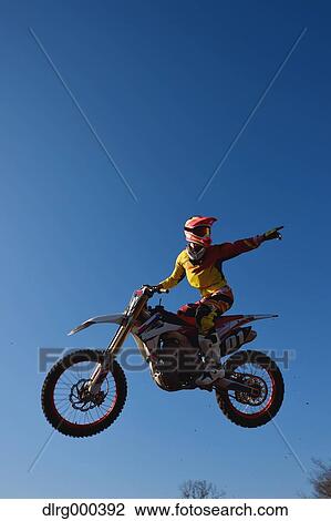 Stock Image - Motocross biker jumping over dirt track. Fotosearch
