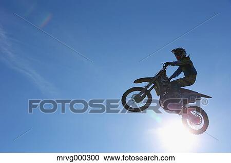Stock Image - Motocross biker jumping over dirt track. Fotosearch
