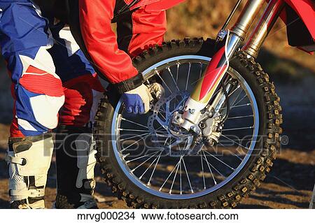 Picture - Motocross biker working on his bike on dirt track. Fotosearch