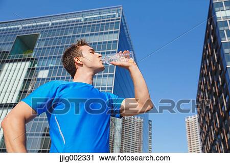 Stock Image - Young Caucasian man drinking water in metropolitan area. Fotosearch