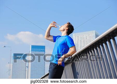 Stock Photo - Young Caucasian man drinking water in metropolitan area. Fotosearch