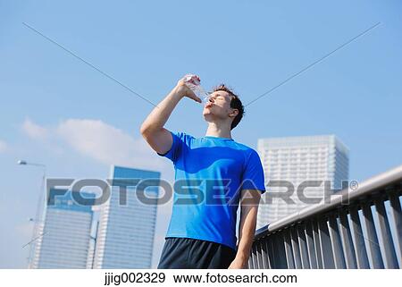 Stock Photo - Young Caucasian man drinking water in metropolitan area. Fotosearch