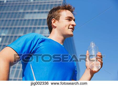 Stock Photograph - Young Caucasian man drinking water in metropolitan area. Fotosearch