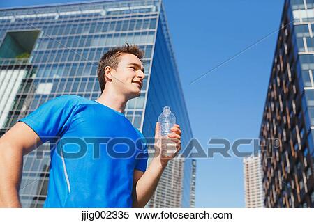 Stock Photography - Young Caucasian man drinking water in metropolitan area. Fotosearch