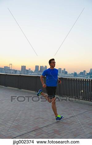 Picture - Young Caucasian man running in metropolitan area. Fotosearch
