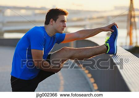 Stock Photograph - Young Caucasian man stretching in metropolitan area. Fotosearch