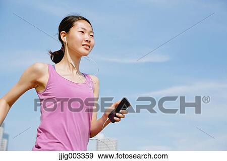 Stock Photo - Young Japanese with smartphone during her run downtown Tokyo. Fotosearch