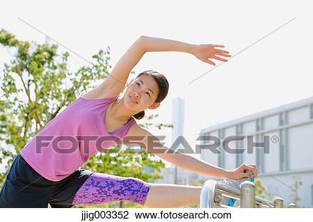 Stock Image - Young Japanese woman stretching before her run downtown Tokyo. Fotosearch