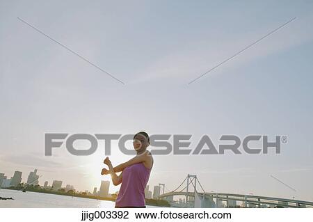 Stock Image - Young Japanese woman stretching before her run downtown Tokyo. Fotosearch