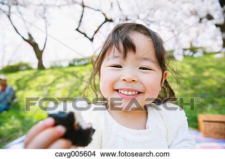 Young smiling Japanese girl enjoying cherry blossoms in a city park View Large Photo Image Picture - Young smiling Japanese girl enjoying cherry blossoms in a city park. Fotosearch
