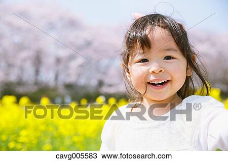 Stock Image - Young smiling Japanese girl enjoying cherry blossoms in a city park. Fotosearch