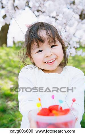 Stock Image - Young smiling Japanese girl enjoying cherry blossoms in a city park. Fotosearch