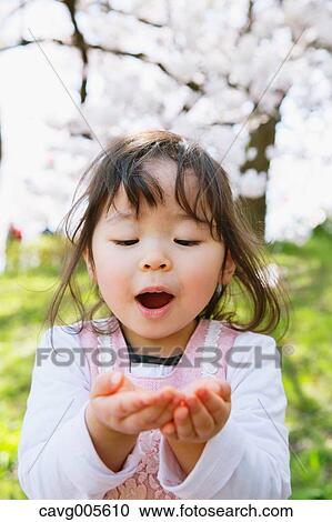 Stock Image - Young smiling Japanese girl enjoying cherry blossoms in a city park. Fotosearch