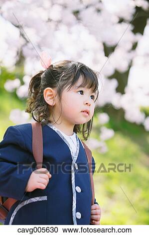 Stock Image - Young smiling Japanese girl enjoying cherry blossoms in a city park. Fotosearch