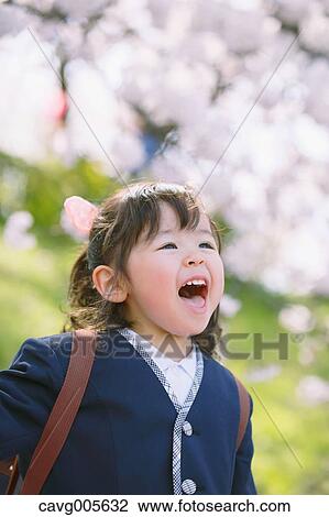 Stock Image - Young smiling Japanese girl enjoying cherry blossoms in a city park. Fotosearch