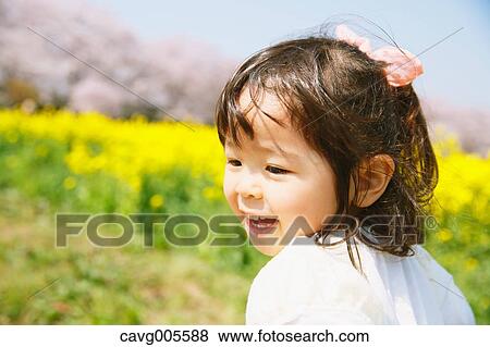 Stock Photo - Young smiling Japanese girl enjoying cherry blossoms in a city park. Fotosearch