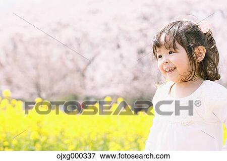 Stock Photo - Young smiling Japanese girl enjoying cherry blossoms in a city park. Fotosearch