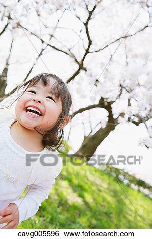 Stock Photograph - Young smiling Japanese girl enjoying cherry blossoms in a city park. Fotosearch