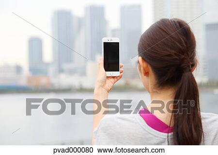 Stock Image - Attractive Japanese woman taking pictures by a river downtown Tokyo, Japan. Fotosearch