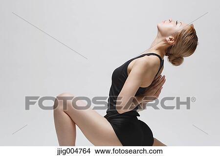 Picture - Attractive young Japanese woman wearing black pants and tank top practicing yoga on white background. Fotosearch