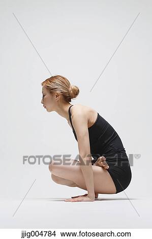 Picture - Attractive young Japanese woman wearing black pants and tank top practicing yoga on white background. Fotosearch